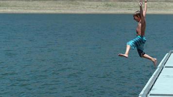 Boy jumping off dock into lake in super slow motion video