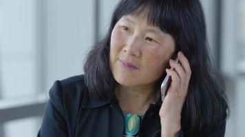 Reife asiatische Geschäftsfrau mit Handy in der Bürolobby