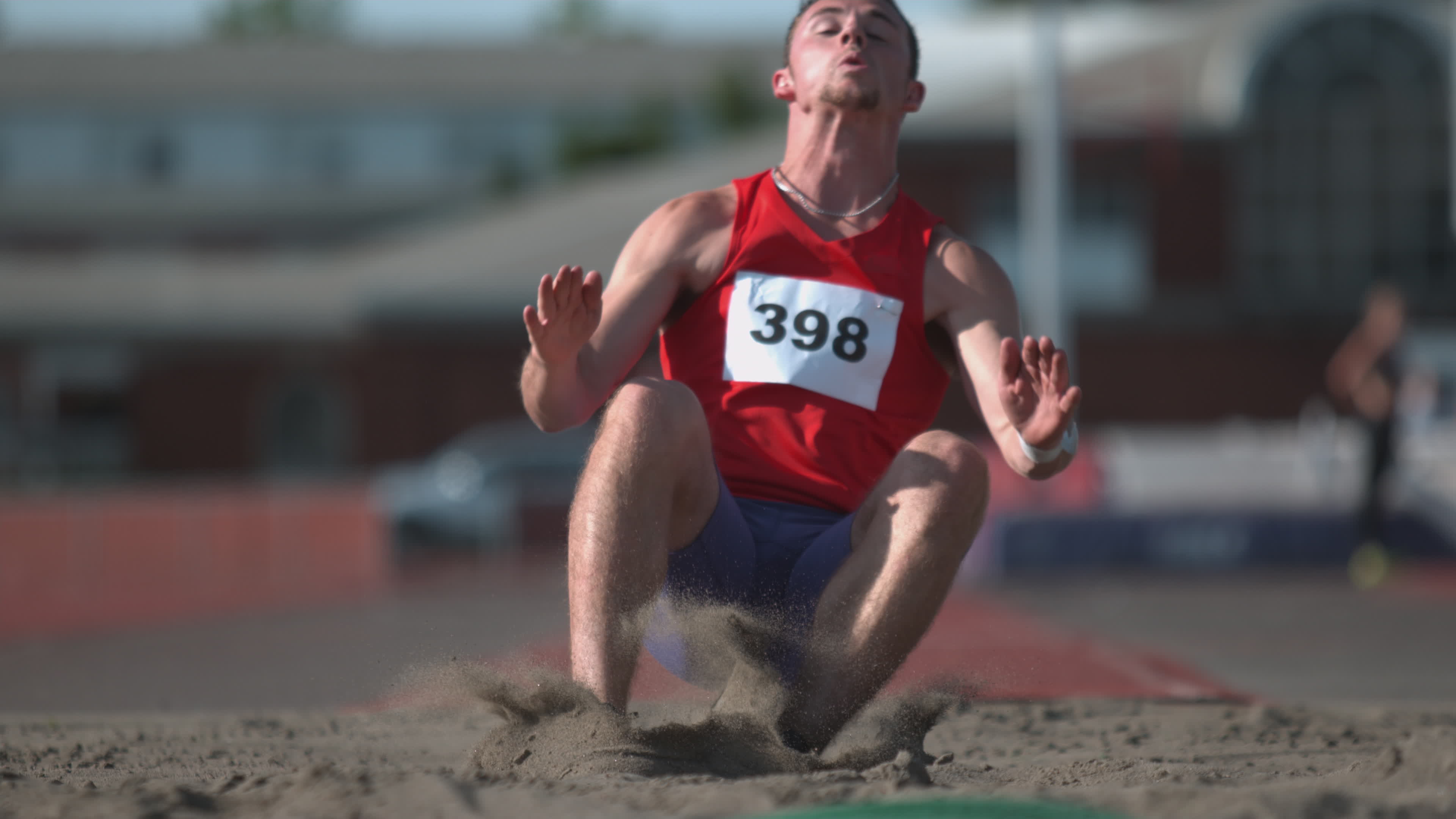 Track athlete landing in sand on long jump in super slow motion, shot