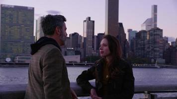 Couple in New York City stand by river talking with skyline in background video