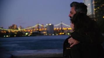 Couple in New York City standing on pier at night with city skyline in background