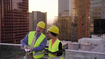 Two construction supervisors look at plans on rooftop video