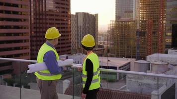 Two construction supervisors look at plans on rooftop