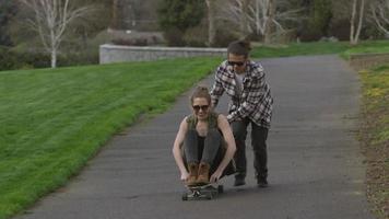 Teen drängt Mädchen auf Skateboard im Park video