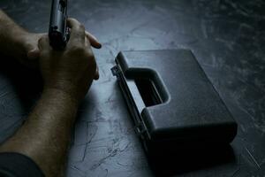 Man hands with weapon and suitcase from under pistol on concrete table photo