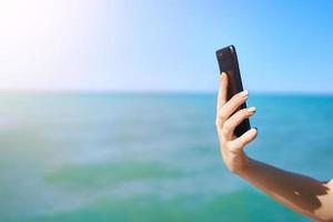 Smartphone in woman hand on sea background photo