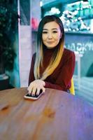 Joven mujer asiática en la mesa de café tiene la mano en el teléfono móvil