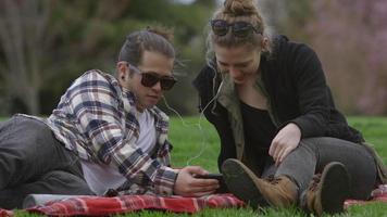 twee jonge mensen in het park op deken die samen naar muziek luisteren video