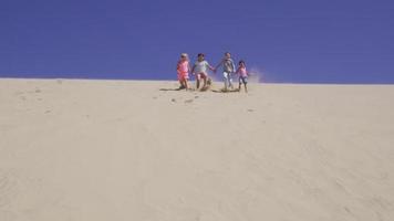 Group of kids running down sand dune at beach