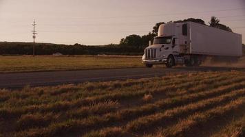 semi caminhão dirigindo pela estrada poeirenta ao pôr do sol. totalmente liberado para uso comercial. video
