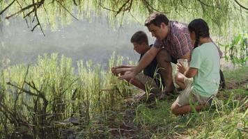 Kids at outdoor school look at pond water with teacher video