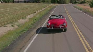 Tracking shot of man driving classic convertible car on country road.  Fully released for commercial use.