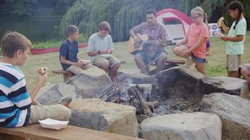 enfants au camp d'été par feu de camp avec chef jouant de la guitare video