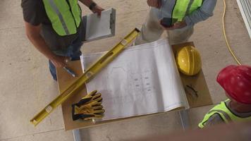 Three construction workers shaking hands over blueprints, overhead shot