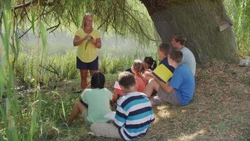 les enfants de l'école en plein air ont une leçon de groupe au bord de l'étang video