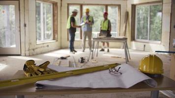 Three construction workers looking over blueprints in background with foreground in focus