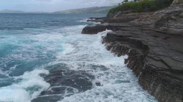 Low angle aerial view of waves crashing cliffs and rocks, Oahu, Hawaii video