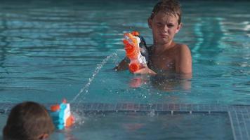 menino esguichando pistola d'água na piscina, super câmera lenta video