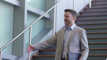 Two businessmen meet and shake hands on stairs of office lobby video