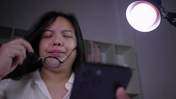 Stressed asian woman sitting and using smartphone working hard trying to resolve the problem in working room at night by searching on Internet and chatting video