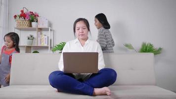 Calm mother sit on couch working on laptop little kids play around peaceful mom relax on sofa use modern computer distracted from noise parenting upbringing concept video