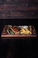 Filete de salmón con papas fritas en una bandeja de madera, hermosa porción, fondo oscuro foto