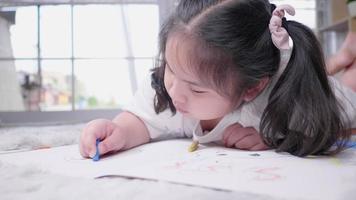 Vista frontal del niño tirado en el suelo pintando con lápices de colores en la sala de estar con mucha felicidad, actividad artística en casa video