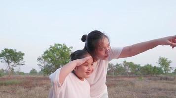 vista frontale della madre asiatica indica e dice alla figlia di guardare lontano nel campo paesaggio forestale poi ragazza che guarda e indica le dita seguire mamma mamma e bambino abbraccio stretto con sorriso e felice video