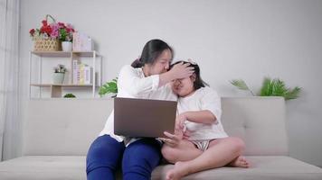 mãe beija filha mãe e filho se divertindo, rindo e assistindo a série dramática da coreia no laptop juntos na sala de estar mãe e filho passando o dia em quarentena video