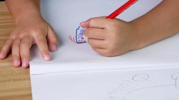 Cerrar la mano del niño dibujando familia feliz en papel con lápices de colores en la mesa en casa