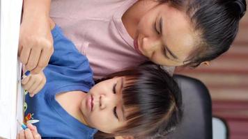 Happy mother and daughter drawing a rainbow on paper at table at home video