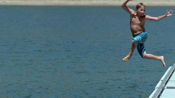 Boy jumping off dock into lake in super slow motion video