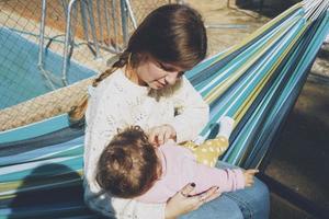 Young woman caring her baby sitting on a hammock photo