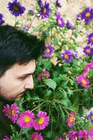 Closeup side view of a young attractive man in calm looking and smelling outdoor flowers photo