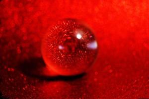 Una macro asombrosa y hermosa de una esfera de cristal sobre un fondo purpurin purpurina roja que parece una gota de agua foto