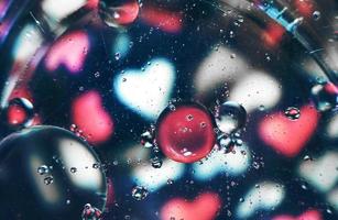 A beautiful and vibrant macro of oil bubbles on water with a blur of white and pink hearts pattern on black background photo