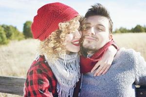 Romántica pareja joven de una hermosa mujer rubia con cabello rizado y con un gorro de lana roja abraza a su novio y un hombre guapo al aire libre foto