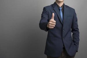 Close up of businessman in blue suit thumbs up on gray background