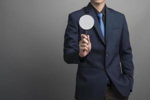 Close up of businessman in blue suit holding magnifier on gray background photo