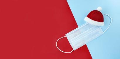 Medical mask and Santa Claus hat on a red, blue background. photo