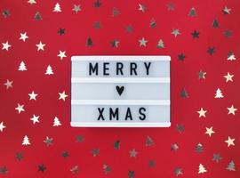 Merry Xmas greeting on light box and confetti on a red background.
