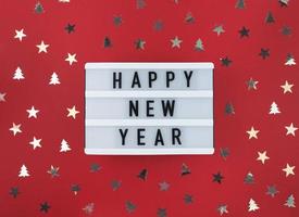 saludo de feliz año nuevo en caja de luz y confeti sobre un fondo rojo. foto