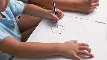 Cerrar la mano de la niña aprendiendo deliberadamente a dibujar a través de la computadora portátil en la sala de estar con la madre. concepto de escuela en casa. educación en línea de jardín de infantes. video