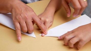 Nahaufnahme der Hand eines Kindermädchens, das mit der Mutter zu Hause die japanische Kunst des Papierfaltens in dekorative Formen und Figuren lernt. video