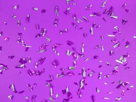 Confetti foil pieces on purple background. Abstract festive backdrop. photo