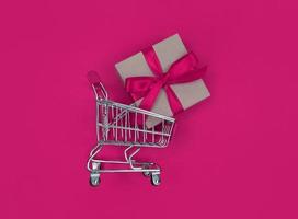 carro de supermercado y caja de regalo sobre fondo rosa. concepto de compras.