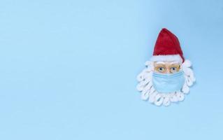 Santa Claus in medical mask on a blue paper. Simple flat lay with copy space.