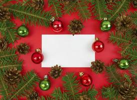 postal navideña con ramas de abeto, conos y adornos sobre un fondo rojo. plano de navidad con espacio de copia.