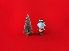 Ceramic statuette of Ox in medical mask and Christmas tree on a red backgroud. Symbol of New Year 2021. photo