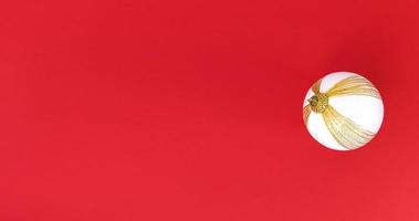 White and gold Christmas tree ball on a red background. Minimalistic holiday flat lay with copy space. photo